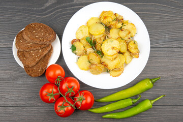 cooked fried potatoes with herbs and vegetables in a white plate on a wooden table