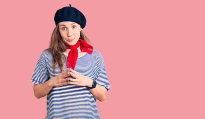 Young beautiful blonde woman wearing french beret and striped t-shirt hands together and fingers crossed smiling relaxed and cheerful. success and optimistic