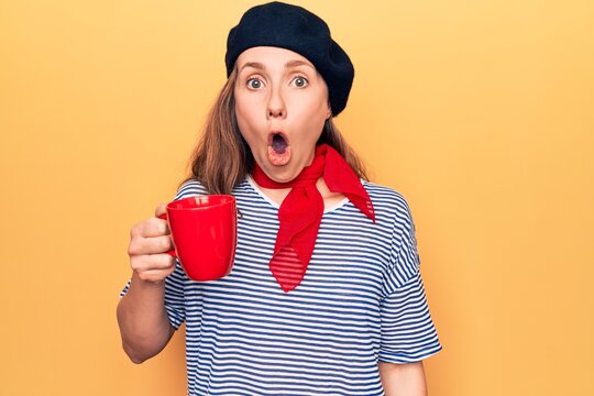 Young beautiful blonde woman wearing fashion beret drinking a cup of coffee scared and amazed with open mouth for surprise, disbelief face