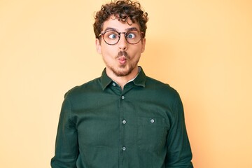 Fototapeta premium Young caucasian man with curly hair wearing casual clothes and glasses making fish face with lips, crazy and comical gesture. funny expression.