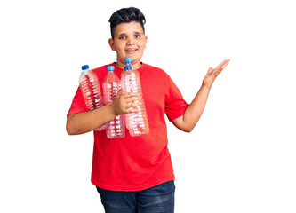 Little boy kid holding recycling plastic bottles celebrating victory with happy smile and winner expression with raised hands