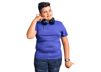 Fototapeta premium Little boy kid listening to music wearing headphones smiling doing phone gesture with hand and fingers like talking on the telephone. communicating concepts.