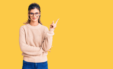 Young beautiful woman wearing casual winter sweater and glasses smiling happy pointing with hand and finger to the side