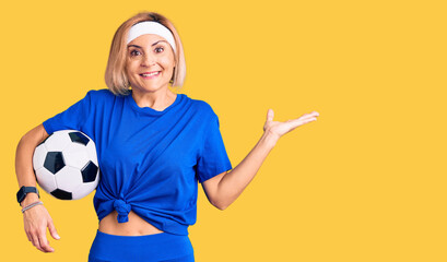 Young blonde woman holding soccer ball celebrating victory with happy smile and winner expression with raised hands