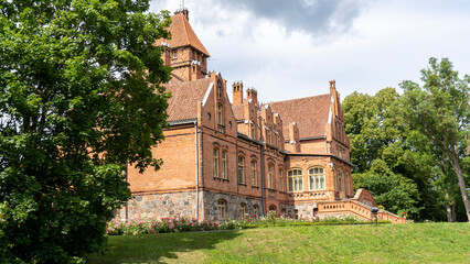 Tume, Latvia_- July 7, 2020: Brick Medieval Jaunmoku Castle at Pond. The Jaunmokas Manor Park. This...