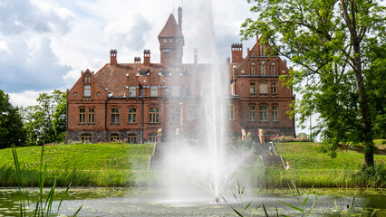 Tume, Latvia_- July 7, 2020: Brick Medieval Jaunmoku Castle at Pond. The Jaunmokas Manor Park. This...