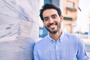 Obraz premium Young hispanic man smiling happy leaning on the wall at the city.
