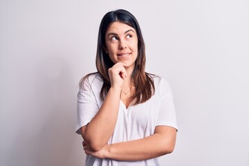 Young beautiful brunette woman wearing casual t-shirt standing over isolated white background thinking concentrated about doubt with finger on chin and looking up wondering