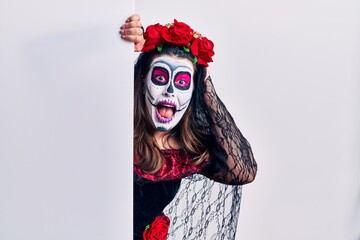 Young woman wearing day of the dead custome holding blank empty banner crazy and scared with hands on head, afraid and surprised of shock with open mouth