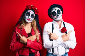 Couple wearing day of the dead costume over red pointing to both sides with fingers, different direction disagree
