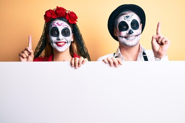Couple wearing day of the dead costume holding blank empty banner smiling with an idea or question pointing finger with happy face, number one
