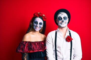 Beautiful couple wearing day of the dead costume smiling happy. Standing with smile on face looking at the camera over isolated red background.