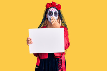 Woman wearing day of the dead costume holding blank empty banner covering mouth with hand, shocked and afraid for mistake. surprised expression