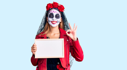 Woman wearing day of the dead costume holding empty white chalkboard doing ok sign with fingers, smiling friendly gesturing excellent symbol