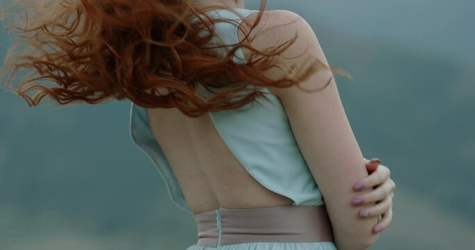 Carefree caucasian girl with red hair with mysterious glance standing against the wind, it blows her dress and hair. Tranquility, inspiration, freedom concept 4k footage