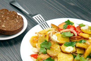 cooked fried potatoes with herbs and vegetables in a white plate on a wooden table