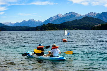 A couple paddling on a lake in Bariloche. Rocks, pines and mountains. Summer day