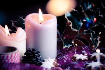 Obraz na płótnie Canvas Christmas background composition on rustic table and fairy lights bokeh, setup made of gingerbread stars and candles on pink cloth, christmas messy table arrangement with candle fire in dark room