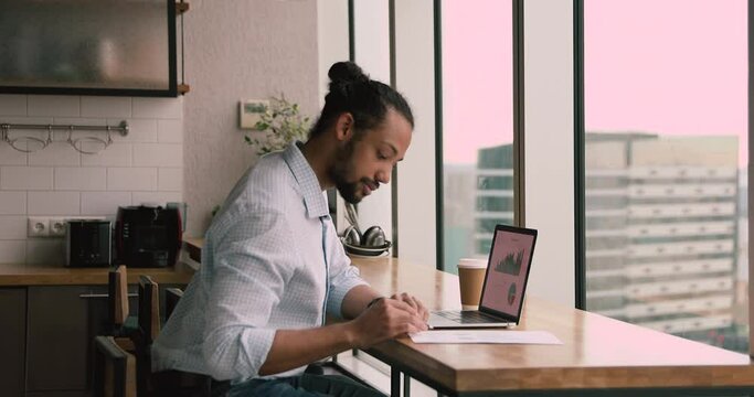 African trader businessman sit in modern kitchen using portable computer with chart and graph on screen, reviewing company financial data, do statistical analysis, making executing trades in equities