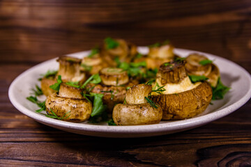 Plate with baked champignons, dill and parsley on a wooden table