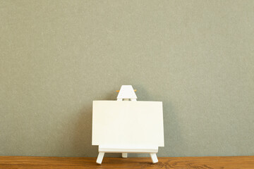 Easel with blank canvas on wooden desk. Khaki green background