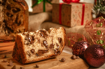 Slice of chocolate panettone  on wooden cutting board with christmas ornaments