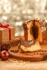 Slice of chocolate panettone  on wooden cutting board with christmas ornaments