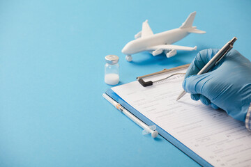 Doctor hand with pen filling in data, on form, with vaccine, syringe, white plane, blue background