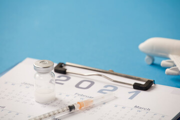 Vaccine with syringe, calendar 2021, and white plane, blue background