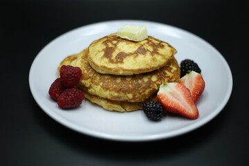 Pancakes stack with different berries and honey isolated on black background