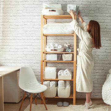 Young Woman In Warm Robe Is Organizing Linen Closet With Neatly Folded Towels, Sheets And Blankets.