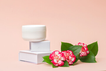 White cosmetic cream jar top with flowers. Side view. Feminine hygienic skincare product on light pink background. Beauty industry concept.