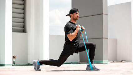 Handsome Latino sports man doing lunge workout with resitance band outdoors in the sun - obrazy, fototapety, plakaty