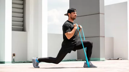 Gardinen Handsome Latino sports man doing lunge workout with resitance band outdoors in the sun © Atstock Productions