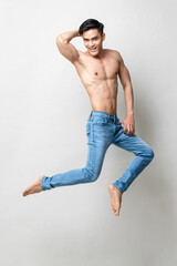 Full length portrait of energetic attractive shirtless Asian man jumping in mid-air in isolated studio light gray background