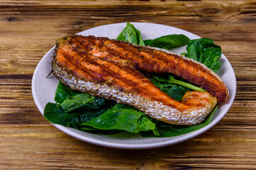Plate with roasted salmon steak and spinach leaves on a wooden table