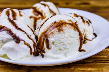 Plate with ice cream balls and chocolate topping on a wooden table