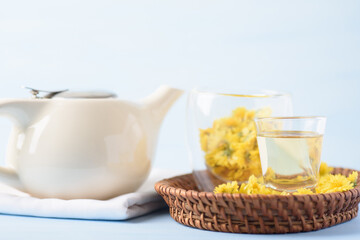 Hot chrysanthemum tea drink in glass cup with fresh flower on light blue background