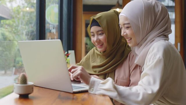 Two Muslim businesswomen use laptop to work in coffee shop. Brainstorm business investment ideas. Hit the hand with happy work is success. Shopping online Or booking accommodation via the website