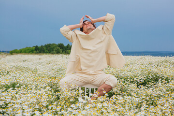 Tall handsome man sitting on a back of a chair in camomile flowers field