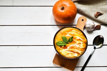 Pumpkin cream soup with fresh basil in bowl and napkin on wooden white background. Top view. Copy space, flat lay. Menu, Food background. Healthy food concept.