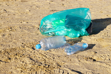 Green plastic bag with garbage on the beach. Plastic bottles.