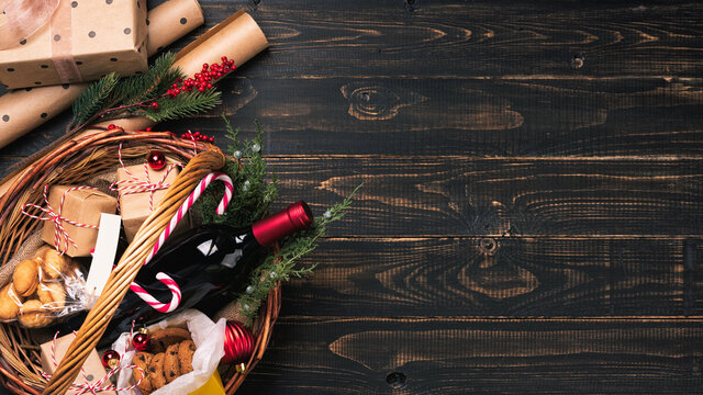 Bottles of red wine in Christmas basket. Mulled wine with gift boxes, cookies and fir-tree ornaments. Dark wooden background