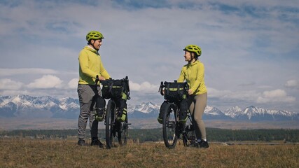 The man and woman travel on mixed terrain cycle touring with bikepacking. The two people journey with bicycle bags. Mountain snow capped.