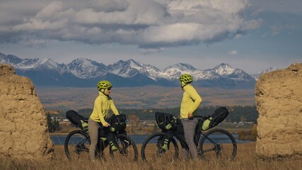 The man and woman travel on mixed terrain cycle touring with bikepacking. The two people journey with bicycle bags. Mountain snow capped, stone arch. © ivandanru