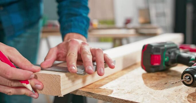 Close up of a hardworking professional carpenter holding a ruler and pencil while making a board center in a carpentry workshop. A bearded DIY enthusiast measures wood. There are a locksmith table and