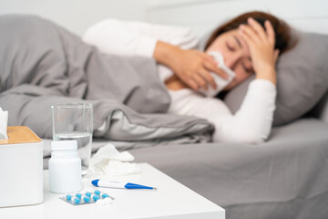 Obraz na płótnie Canvas pill and glasses of water on the table woman suffering headache, fever and flu lying in bed background.