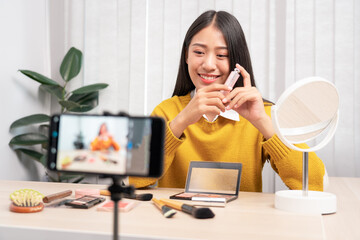 Beautiful asian woman blogger using camera phone recording vlog video live streaming and applying makeup for review cosmetics at home