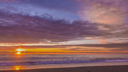 A blazing sunset over the Black Sea. The sun shines through the clouds, painting them orange and scarlet. Waves foaming on the beach. Sunny path on the water and on the sand. Russia
