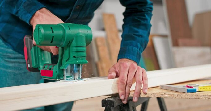 Young carpenter cuts an osb board with a jigsaw. Craftsman's hands in cloth protective gloves. The jigsaw blade cuts precisely.